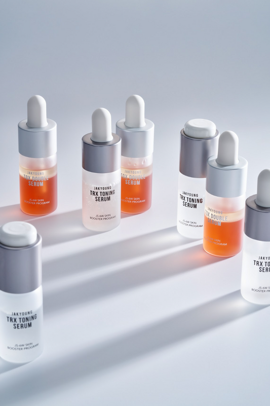 Six skincare dropper bottles arranged on a light gray surface with soft shadows. The bottles contain orange and white liquids.