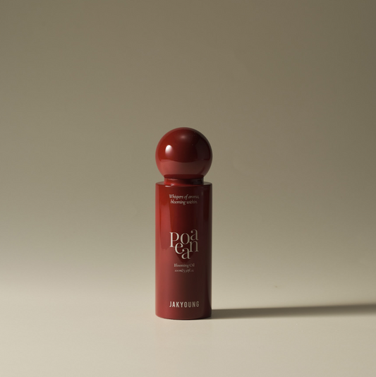 A dark red cylindrical cosmetic bottle with a matching spherical cap, standing on a neutral beige surface against a matching beige background.