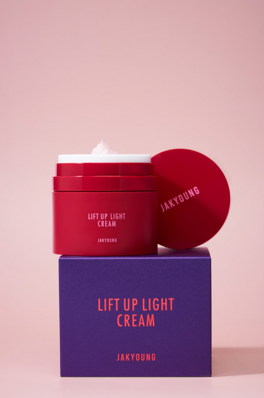 Jakyoung Lift Up Light Cream in a red jar with its lid leaning against it, displayed on top of a purple box against a soft pink background.